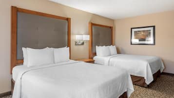 A hotel room with two beds, a nightstand, a wall-mounted lamp, and a framed picture on the wall.