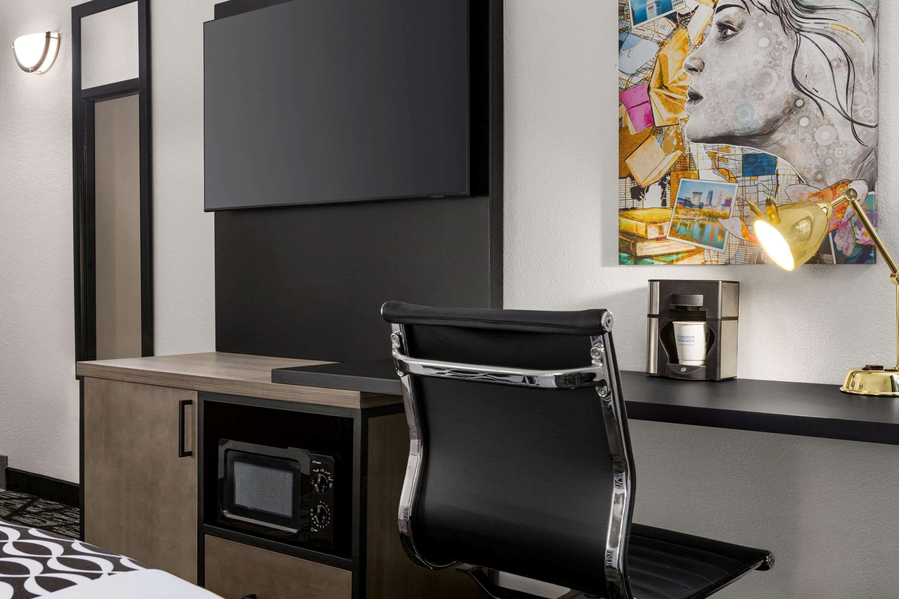 A modern hotel room with a black leather chair, a flat-screen TV, a coffee machine, and a wall art piece.