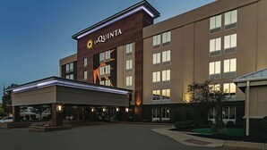 Un hotel con un llamativo letrero de 'La Quinta', un acceso cubierto y una zona ajardinada con un pequeño estanque.