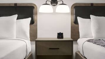 Une chambre d’hôtel avec deux lits, une table de chevet avec une horloge et un luminaire fixé au mur.