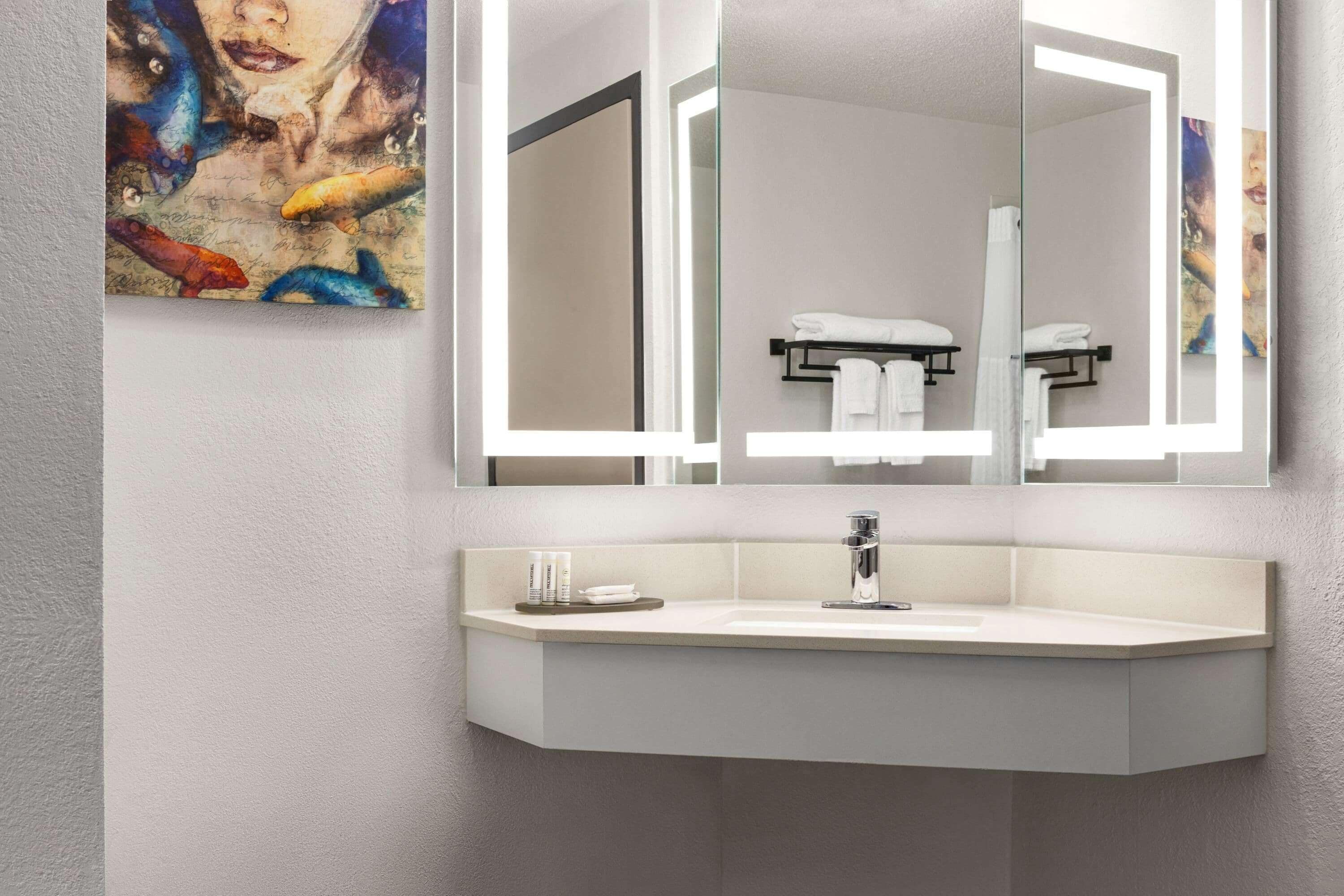 A modern bathroom with a large mirror, a white sink, and a towel rack.