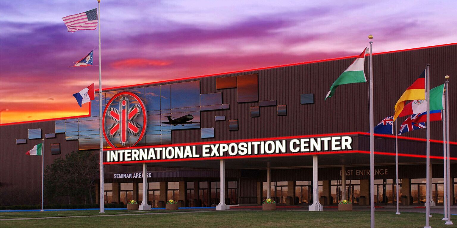 Un centre d’exposition international doté d’une façade moderne, de nombreux drapeaux et surplombé d’un ciel dégagé.
