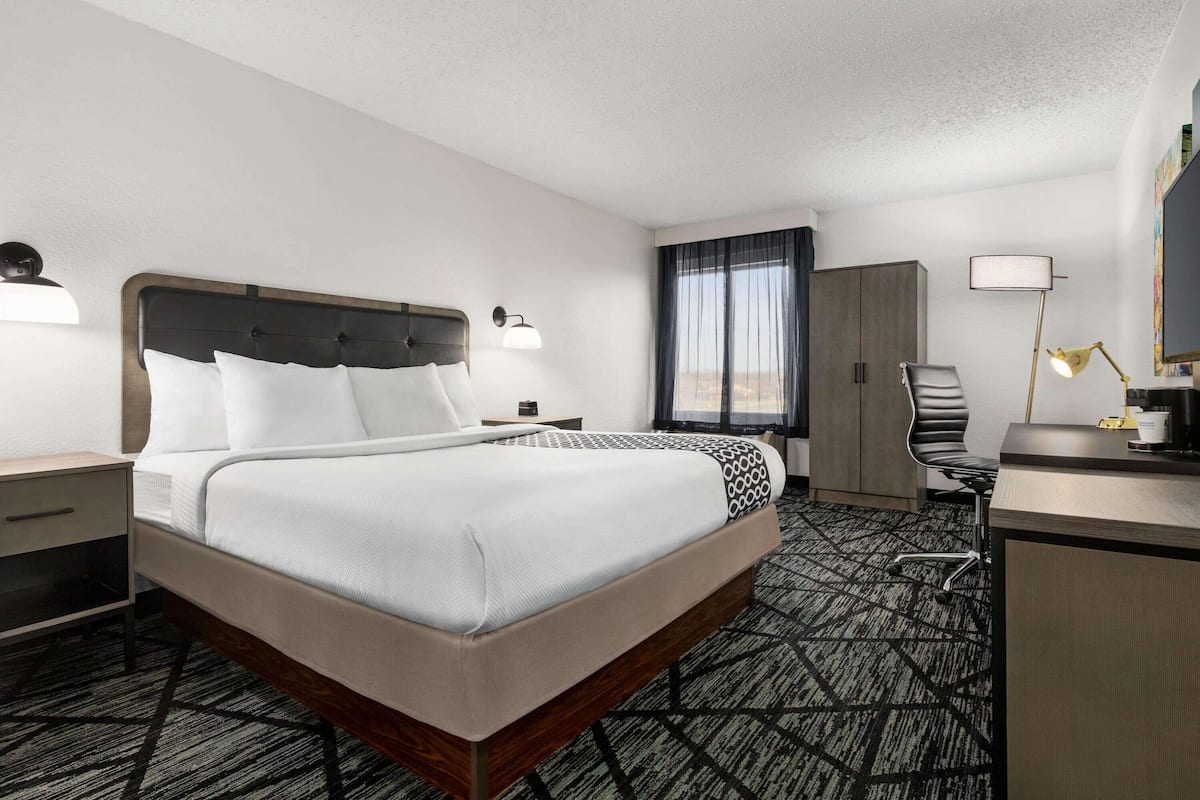 Una habitación de hotel con una cama grande, un escritorio con silla, un armario y una ventana con cortinas.
