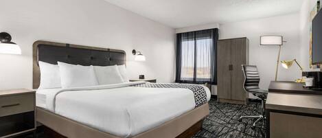Hotelkamer met een groot bed, een bureau met stoel, een garderobe en een raam met gordijnen.