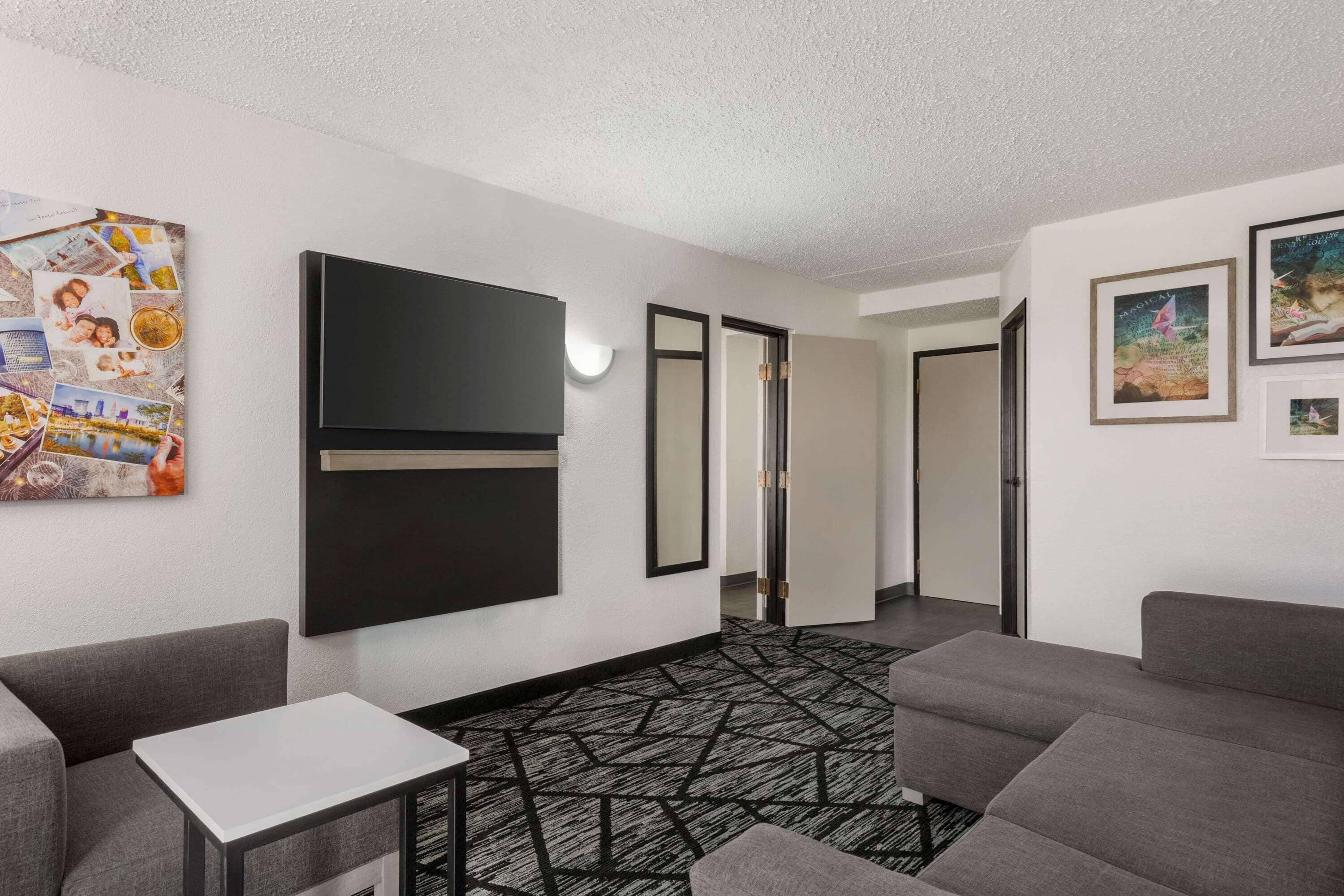 A modern hotel room with a large flat-screen TV, a small white table, and a patterned carpet.