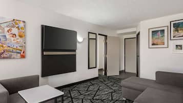 A modern hotel room with a large flat-screen TV, a small white table, and a patterned carpet.