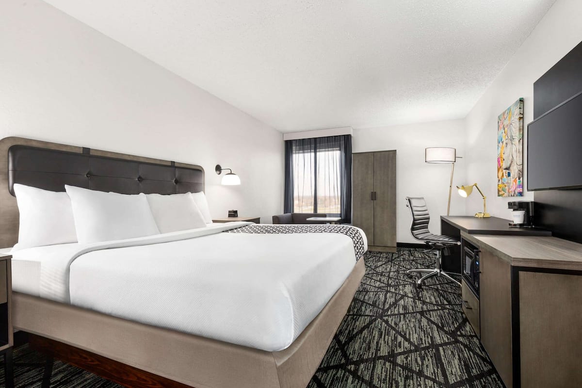 Habitación de hotel con una cama grande, un escritorio, una silla, un televisor y una ventana con cortinas.