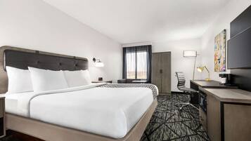 Habitación de hotel con una cama grande, un escritorio, una silla, un televisor y una ventana con cortinas.