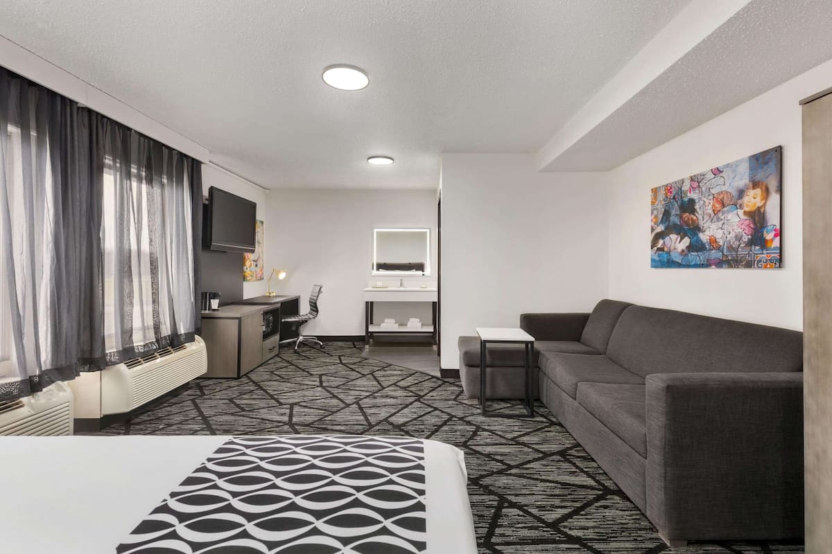 Habitación de hotel con cama, sofá, escritorio con silla, televisor, un cuadro en la pared y alfombra estampada.
