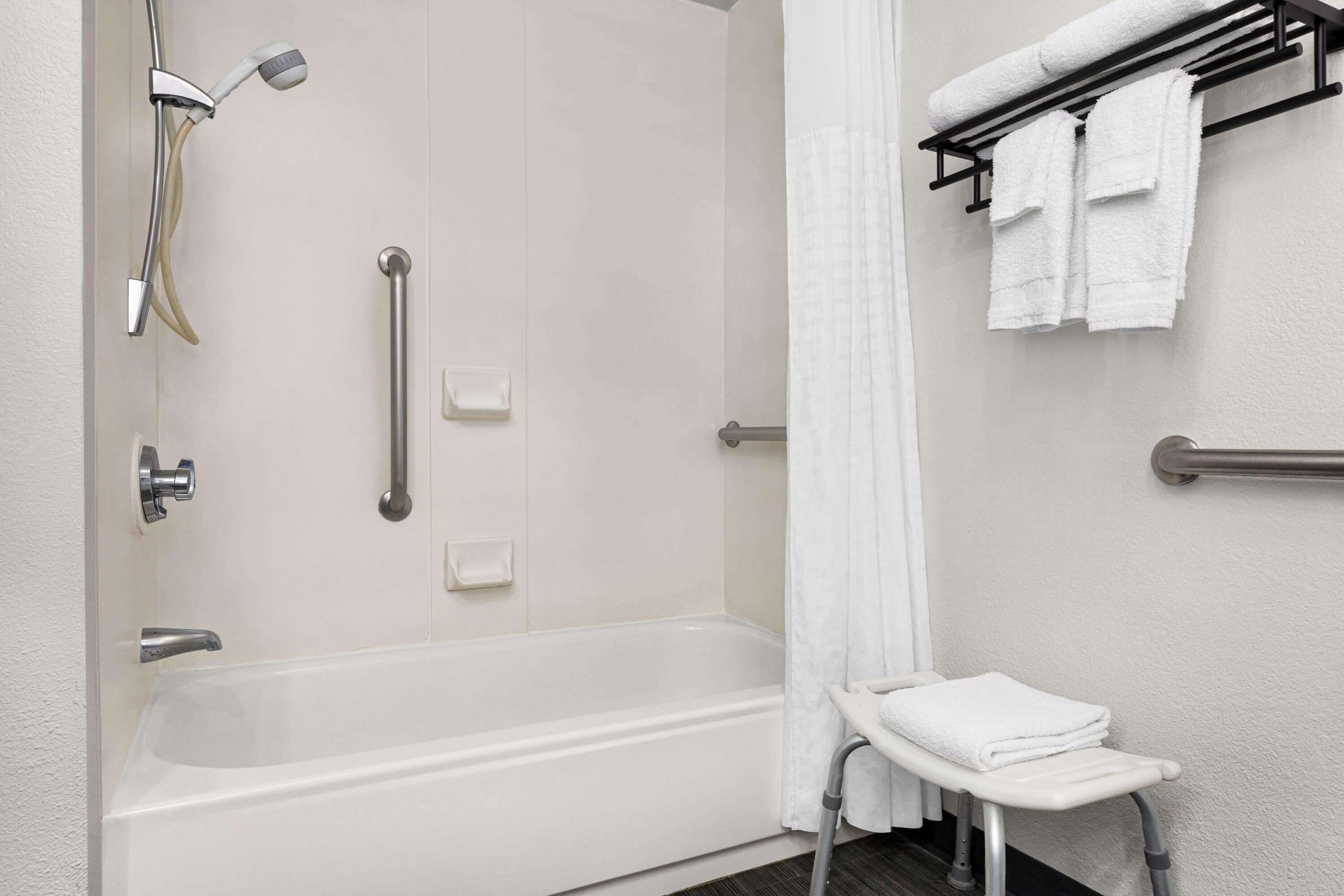 A modern bathroom with a walk-in shower, grab bars, a towel rack, and a wheelchair-accessible bench.
