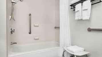 A modern bathroom with a walk-in shower, grab bars, a towel rack, and a wheelchair-accessible bench.
