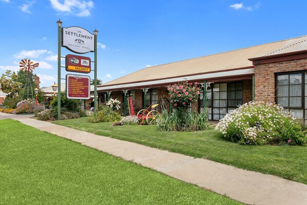 A historic hotel with a sign indicating availability, a windmill, and a well-maintained garden. - The Settlement Historic Hotel (Echuca)