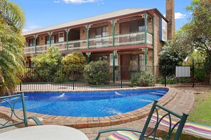 A two-story building with a swimming pool, surrounded by greenery and a fence. - The Settlement Historic Hotel (Echuca)