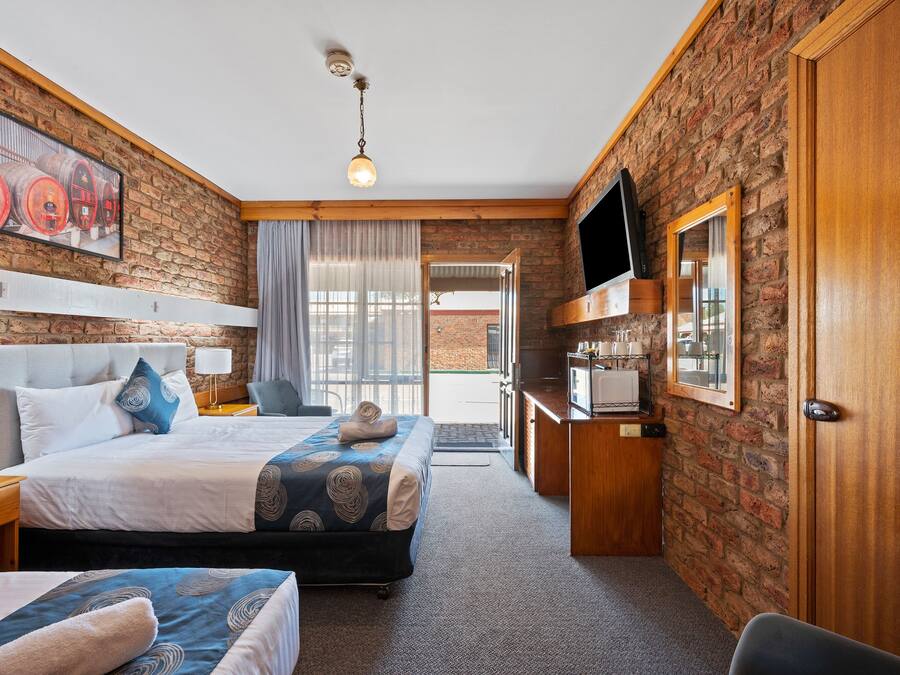 Een hotelkamer met een bakstenen muur, een bed met hoofdeinde, een bureau en een televisie, en een deur.