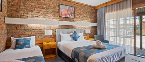 Habitación de hotel con pared de ladrillo, dos camas con cabeceros iguales, un ventanal con cortinas y un cuadro sobre las camas.