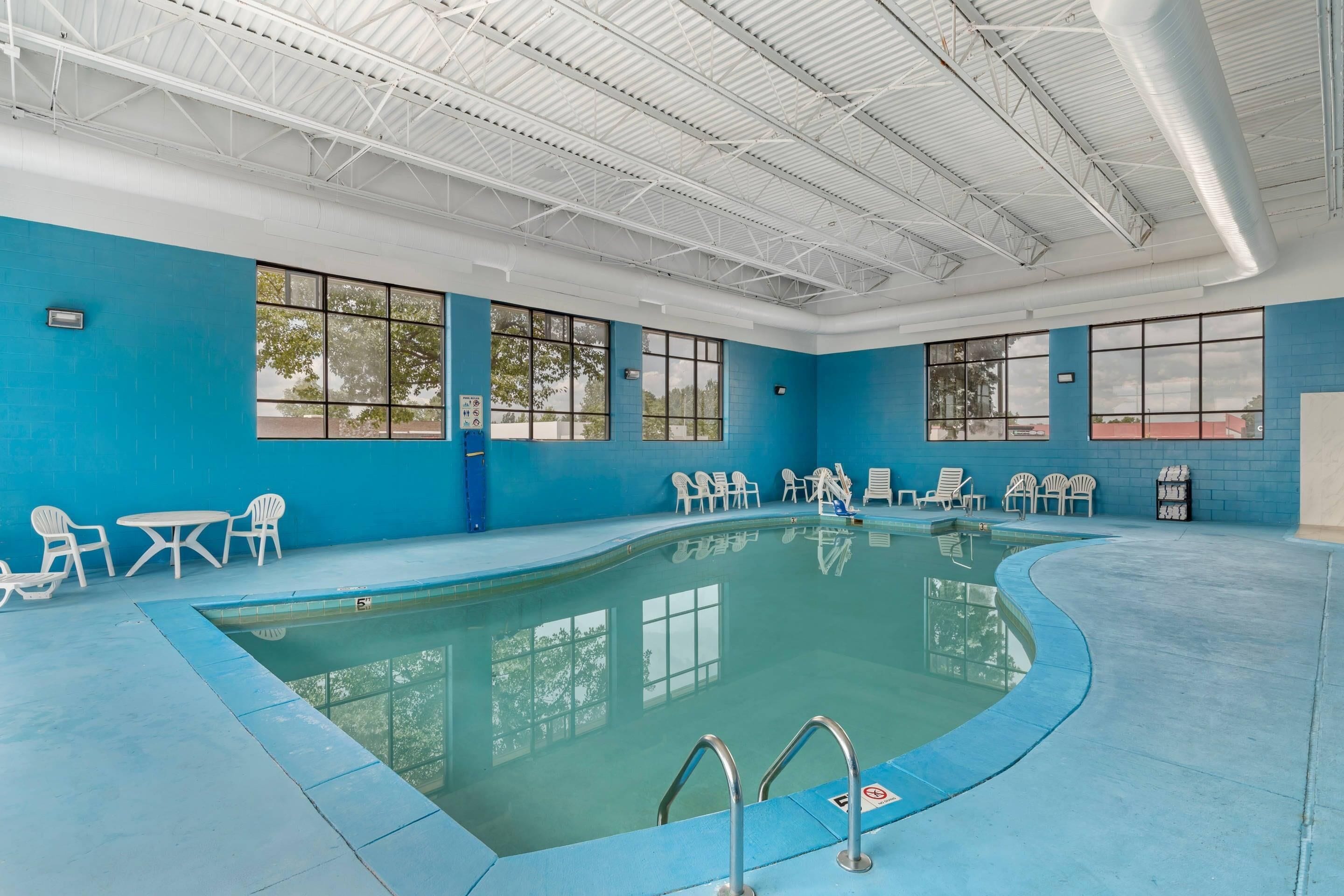 An indoor swimming pool with clear blue walls, large windows, and multiple lounge chairs.