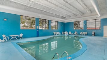 An indoor swimming pool with clear blue walls, large windows, and multiple lounge chairs.