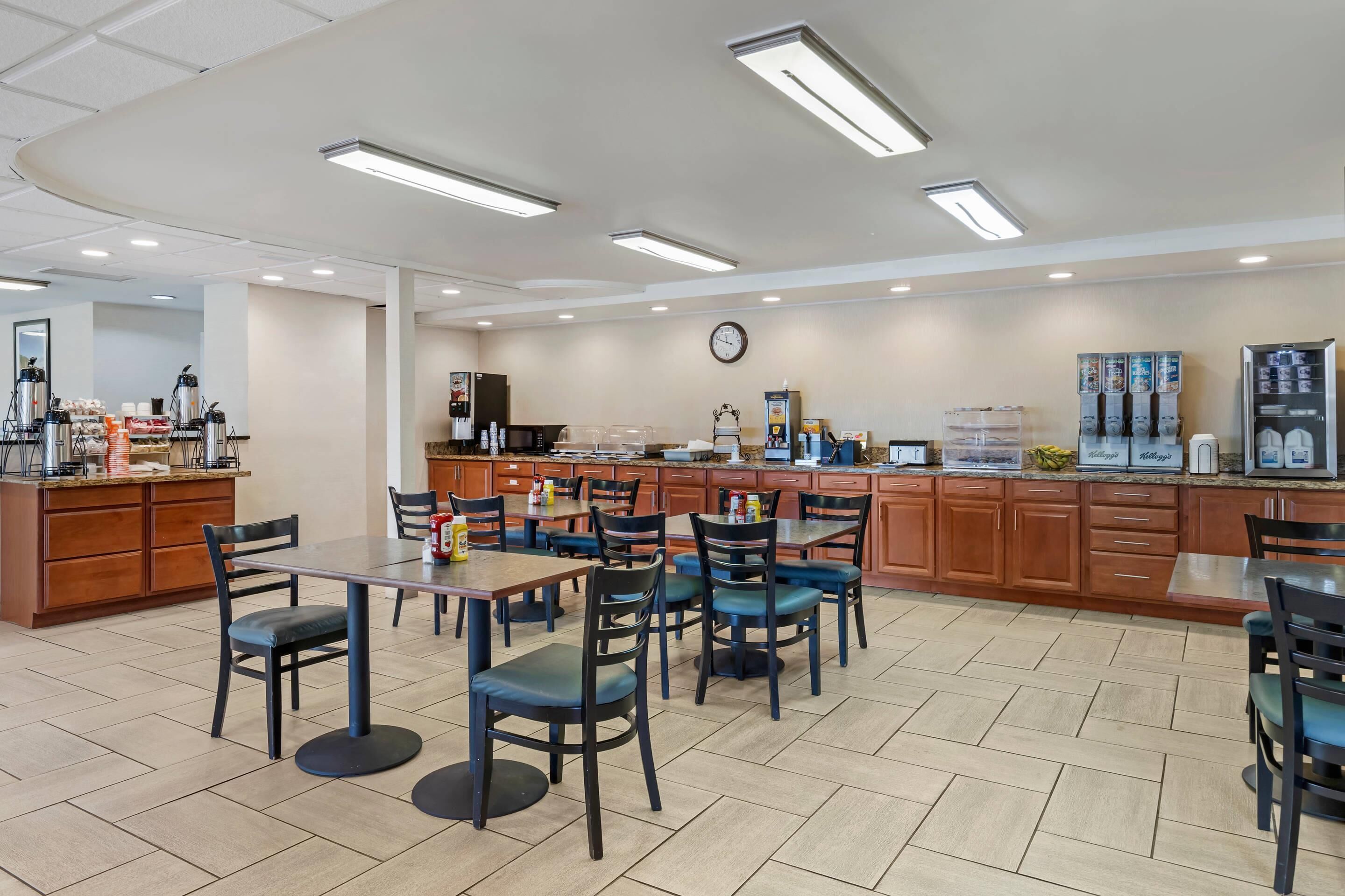 Un grand espace dédié à la salle à manger, avec plusieurs tables et chaises, un coin cuisine équipé d’appareils électroménagers et une horloge au mur.