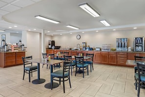 A spacious dining area with multiple tables and chairs, a kitchen area with appliances, and a clock on the wall.