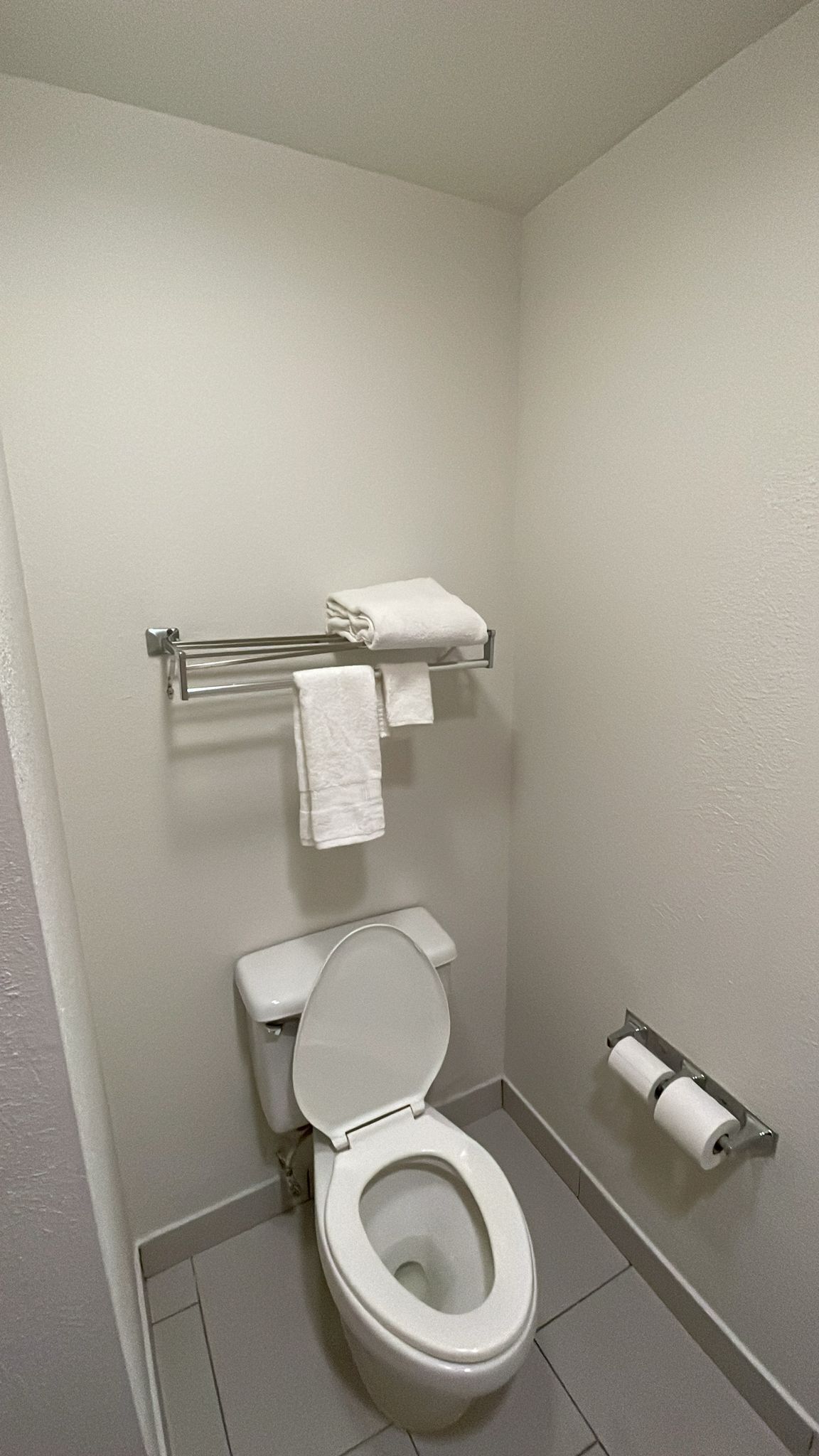 Ein kleines, sauberes Badezimmer mit Toilette, Handtuchhalter mit gefalteten Handtüchern und Toilettenpapierhalter.
