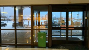 A building entrance with glass doors, a green recycling bin, and an exit sign. - Clarion Inn I-94 near Expo Center (Kalamazoo)