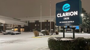 A hotel sign for Clarion Inn by Choice Hotels with a modern building in the background. - Clarion Inn I-94 near Expo Center (Kalamazoo)