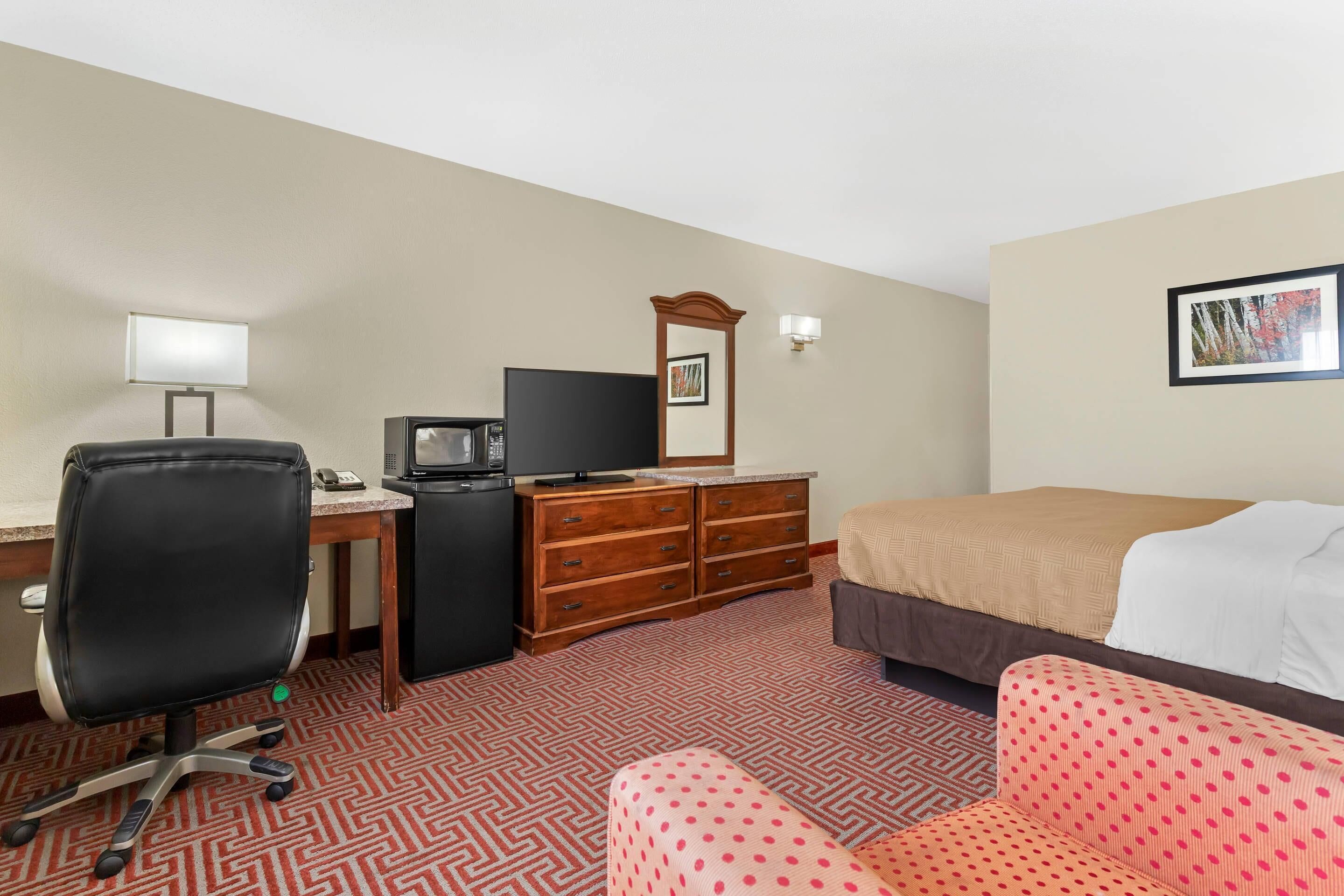 Een hotelkamer met een bureau, een televisie, een kaptafel, een bed en een stoel.