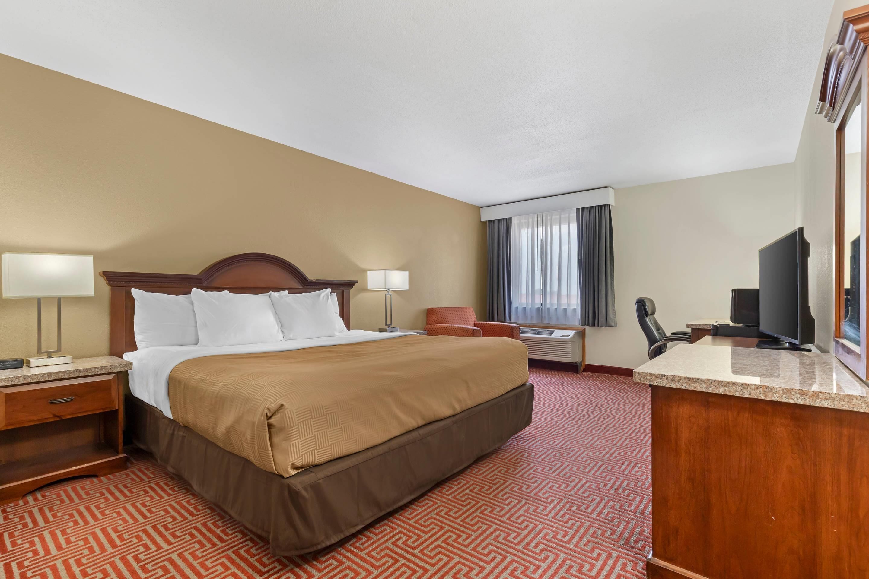A hotel room with a bed, a desk, a chair, a television, and a window with curtains.