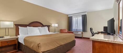 A hotel room with a bed, a desk, a chair, a television, and a window with curtains.