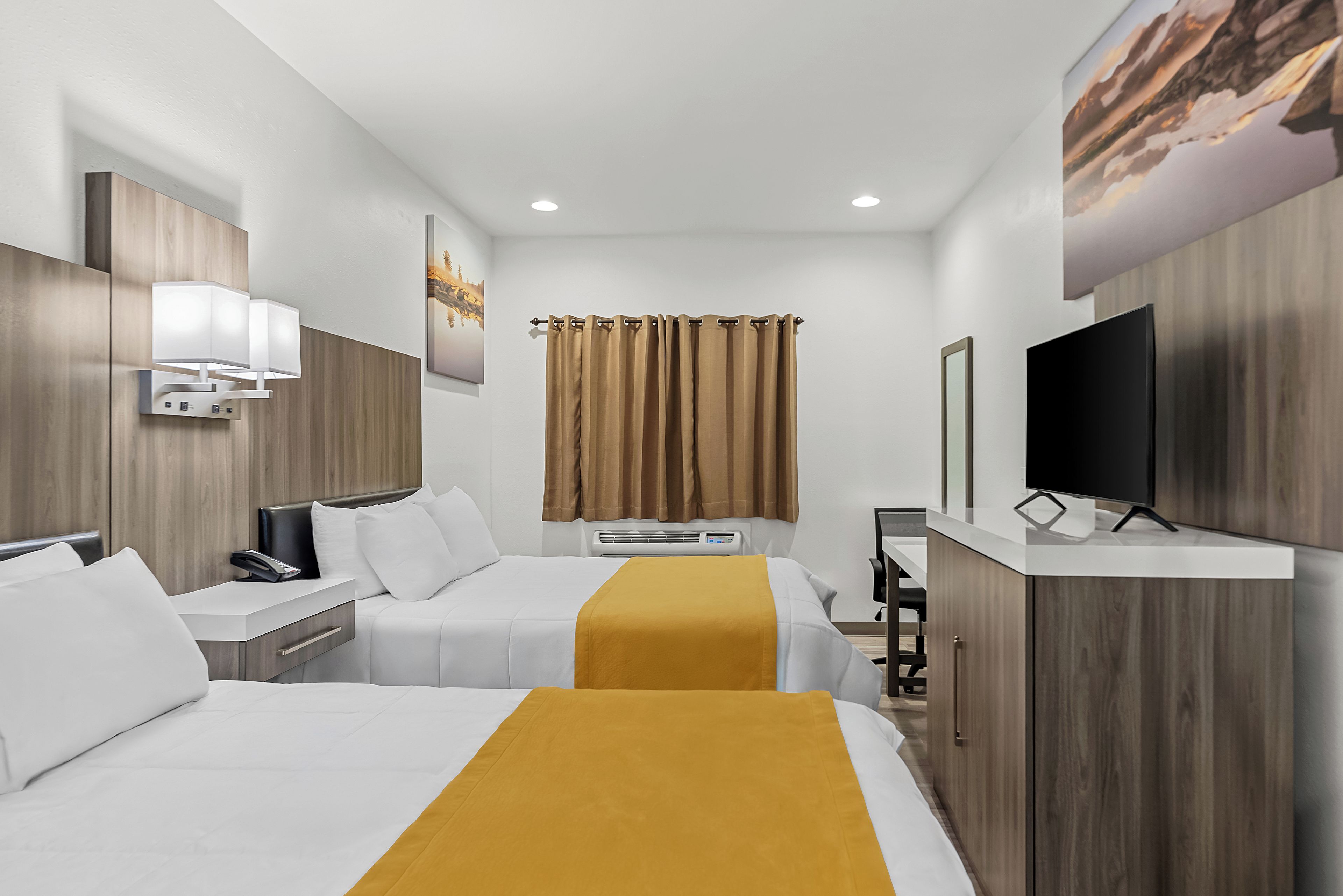 A hotel room with two beds, a TV, a desk, and a painting on the wall.