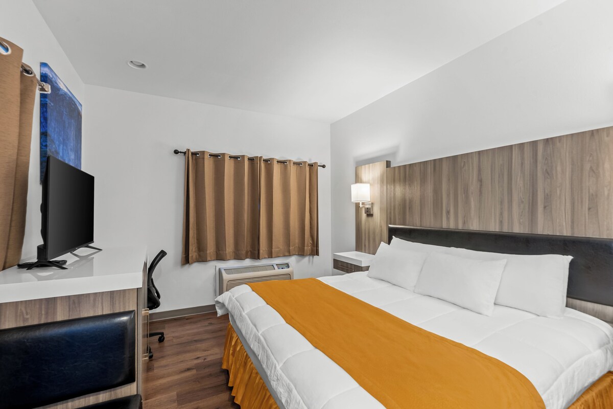 A hotel room with a bed, a desk with a computer, a chair, a television, and a window with curtains.
