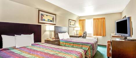 A hotel room with two beds, a desk, a television, and a window with curtains.