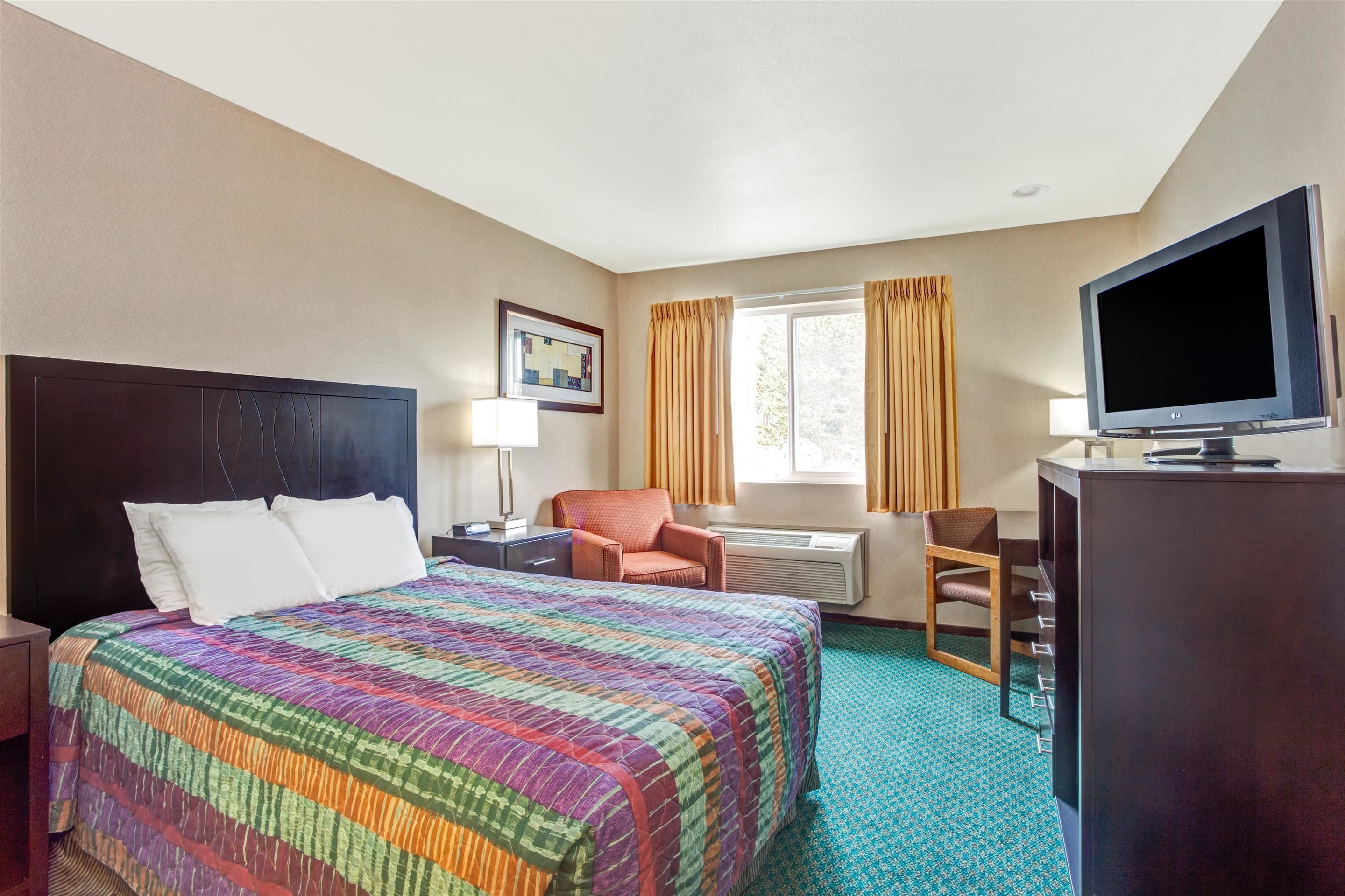 Une chambre d’hôtel avec un grand lit, un bureau avec une télévision, une chaise et une fenêtre avec des rideaux.