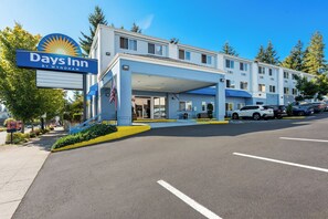 A Days Inn by Wyndham hotel with a covered entrance, multiple parking spaces, and a clear sky. - Days Inn by Wyndham Seattle Aurora (Shoreline)