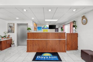 A reception desk with a Days Inn sign, a wooden counter, and a reception area with a door and potted plants. - Days Inn by Wyndham Seattle Aurora (Shoreline)