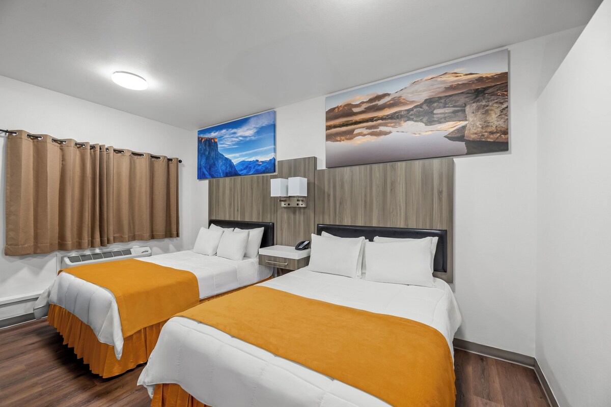 A hotel room with two beds, a large window, a painting, and a ceiling light.