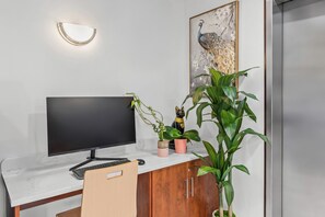 A modern office desk with a flat-screen monitor, keyboard, and a chair. There are potted plants and a decorative item on the desk. - Days Inn by Wyndham Seattle Aurora (Shoreline)