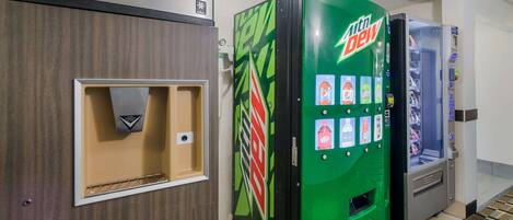 A hotel room with a Mountain Dew vending machine, a minibar, and a small seating area.