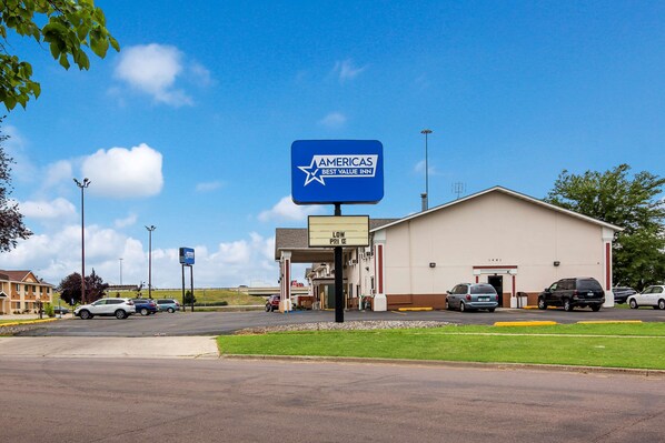 A hotel entrance with a sign indicating it is a Best Value Inn, a parking lot with several cars, and a building with a beige facade.