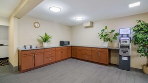 A kitchen with wooden cabinets, a microwave, an ATM, and potted plants. - Americas Best Value Inn Fargo (Fargo)