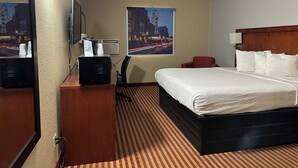 A hotel room with a bed, a desk with a computer, a chair, a mirror, and two posters on the wall. - Americas Best Value Inn Fargo (Fargo)