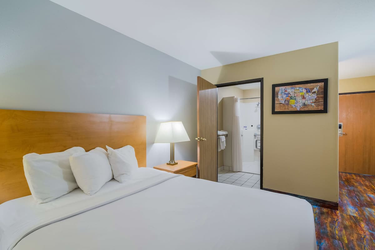 Hotellihuone, jossa on suuri sänky, yöpöytä lampun kanssa, avoimesta ovesta näkyvä kylpyhuone ja Yhdysvaltojen kartta seinällä.