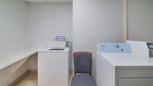 A laundry room with a washing machine, a dryer, and a chair. - Americas Best Value Inn Fargo (Fargo)