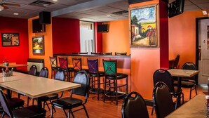 Un restaurante con una decoración en tonos rojos y anaranjados, varias mesas y sillas, y un cuadro en la pared.
