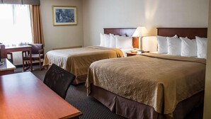 Una habitación de hotel con dos camas, un escritorio, una silla y una lámpara.