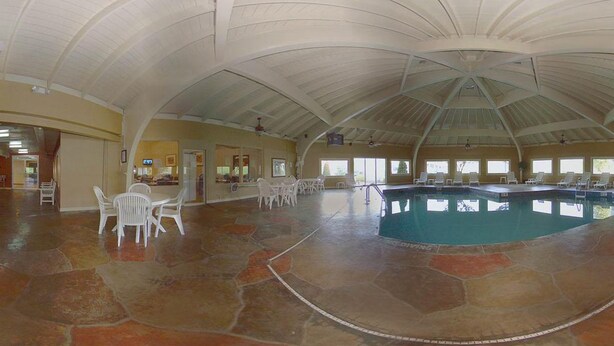 Una amplia piscina interior con techo curvo, suelo de piedra y sillones blancos para relajarse.