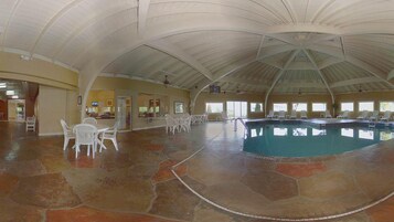 Una amplia piscina interior con techo curvo, suelo de piedra y sillones blancos para relajarse.