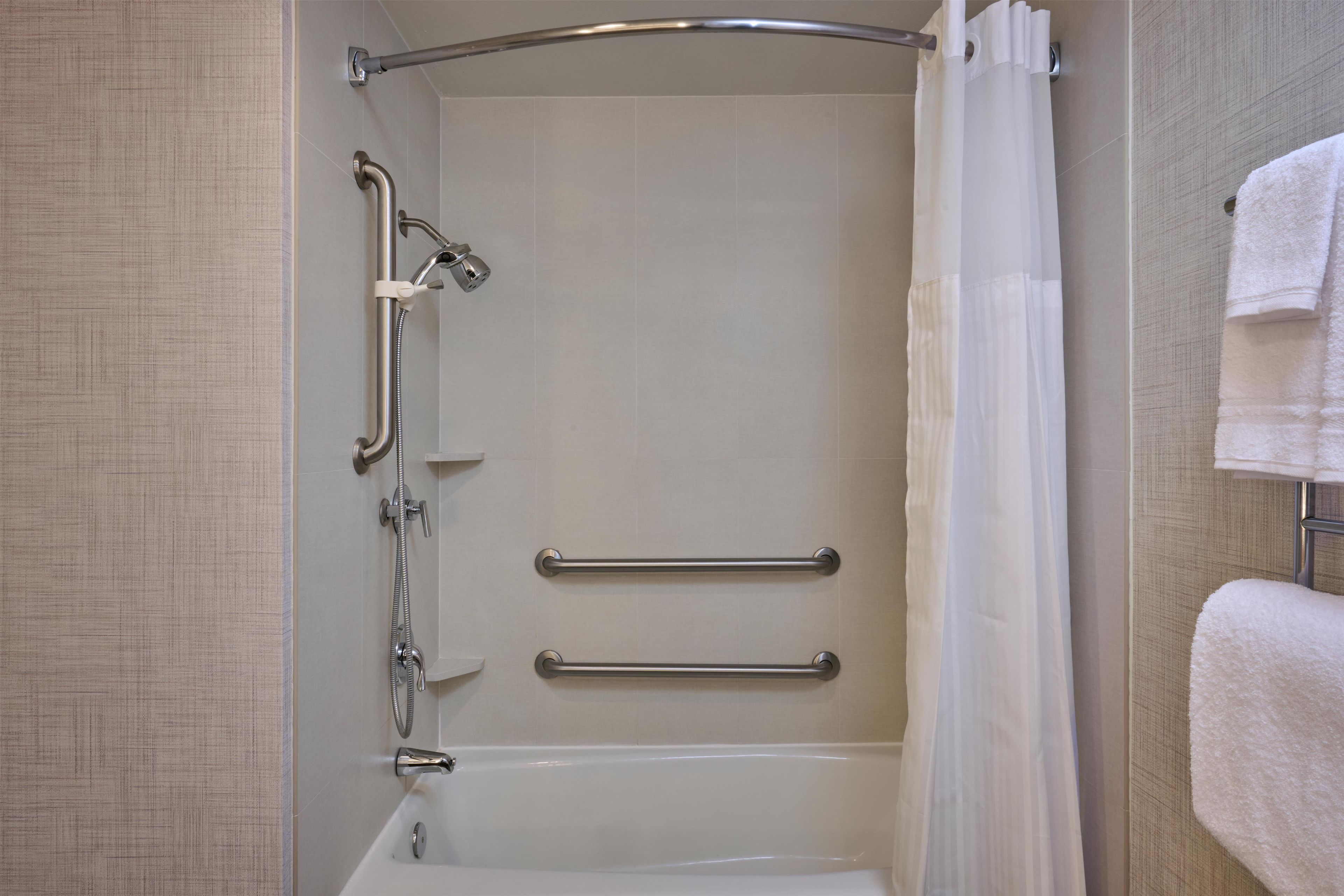 A shower with a grab bar, a white bathtub, and a towel rack.