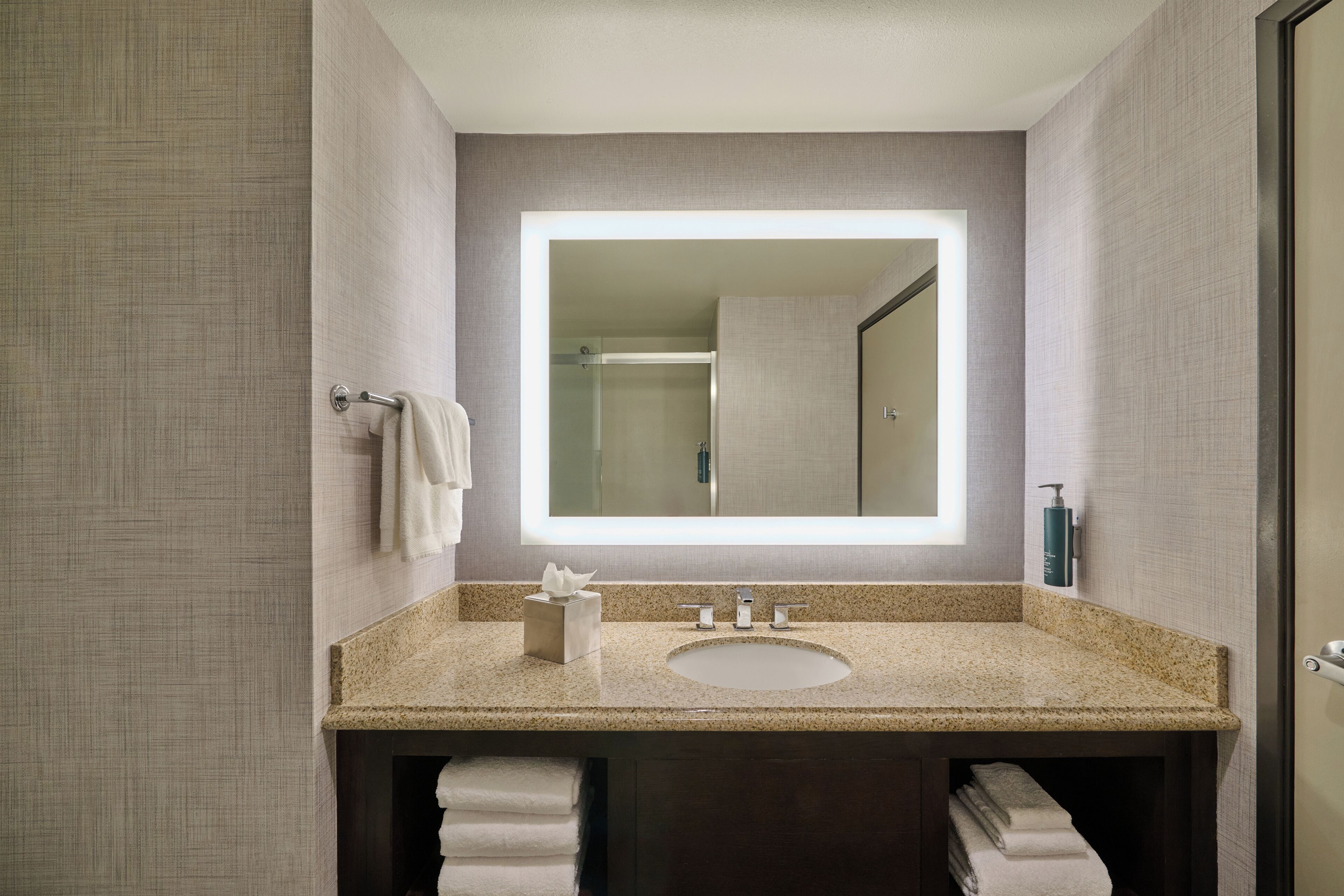 Un baño moderno con encimera de granito, un espejo grande y un lavabo empotrado.