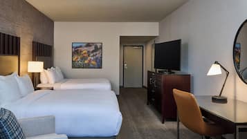 A hotel room with two beds, a desk, a chair, a TV, a dresser, and a painting on the wall.